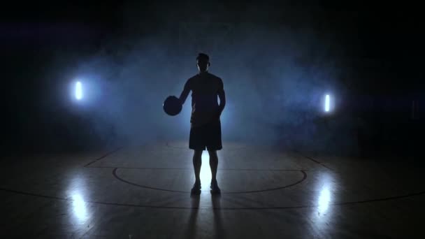 O jogador de basquete vai para a câmera e bate a bola no chão, em seguida, pára e segura a bola olhando para a câmera — Vídeo de Stock