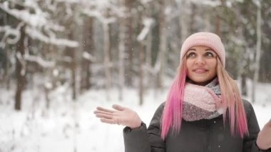 Ağır çekim, ormanda kar düşüş izlerken ve gökyüzü ve doğrudan kameraya gülümseyen kadın kış.