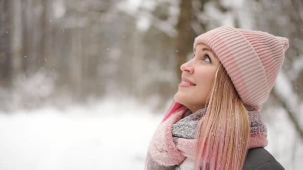 ジャケットとスローモーションで帽子の女は雪を見て、笑みを浮かべて雪片をキャッチ — ストック動画