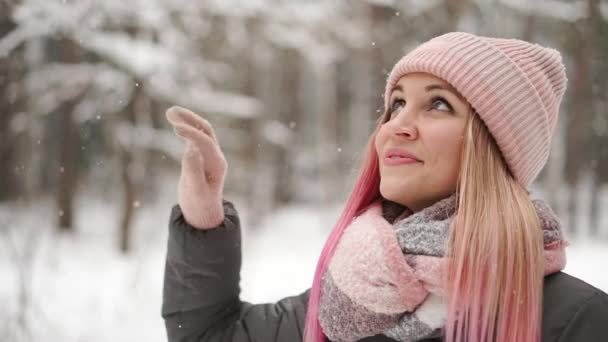 Αργή κίνηση, γυναίκα του χειμώνα στο δάσος βλέποντας την πτώση χιονιού και χαμογελάει κοιτάζοντας τον ουρανό και απευθείας στην κάμερα. — Αρχείο Βίντεο