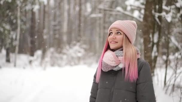 Медленное движение, зимняя женщина в лесу наблюдает, как падает снег и улыбается, глядя на небо и прямо в камеру . — стоковое видео