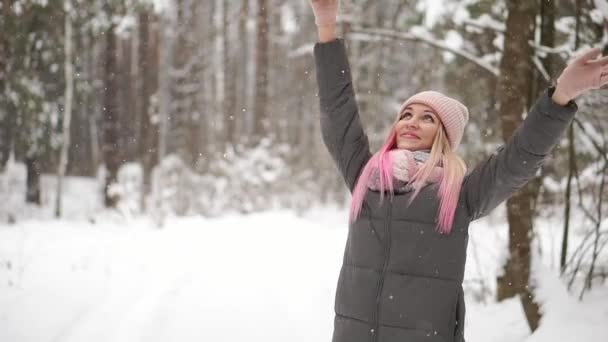 Movimento lento, uma mulher de chapéu e cachecol no inverno na floresta segurando neve em suas mãos e soprando na câmera joga neve . — Vídeo de Stock