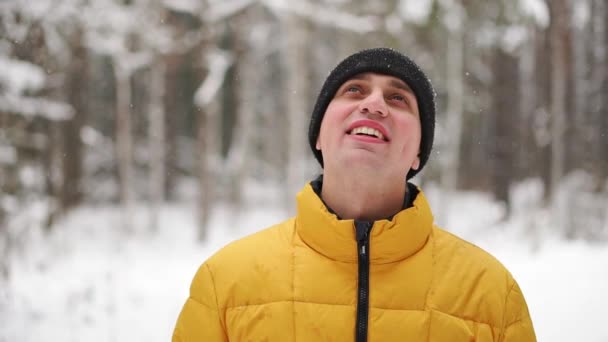 Человек в жёлтой куртке зимой смотрит на снег в лесу и улыбается в замедленной съемке. — стоковое видео