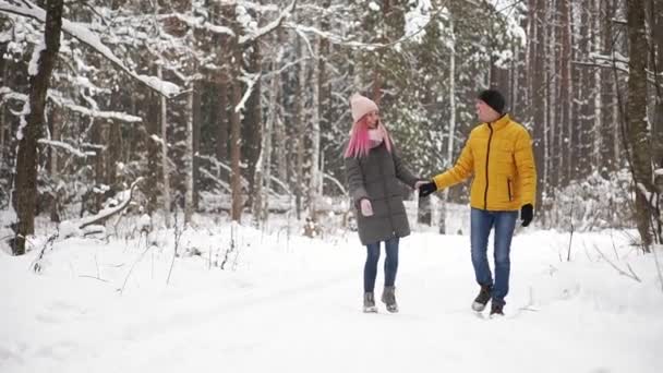 Ένας άνθρωπος σε ένα κίτρινο σακάκι και ένα κορίτσι σε ένα καπέλο και φουλάρι με τα πόδια μέσα στο δάσος του χειμώνα κατά τη διάρκεια μια χιονόπτωση γελούν και να χαμογελούν σε κάθε άλλο Χριστούγεννα σε αργή κίνηση — Αρχείο Βίντεο