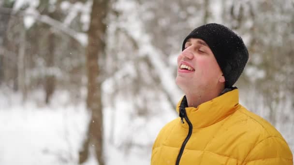 Un uomo in giacca gialla guarda la neve d'inverno nel bosco e sorride al rallentatore — Video Stock