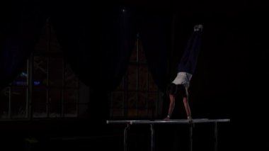 Erkek jimnastikçi acrobat paralel bar flips paylaşımı ve yere iniş yavaş karanlık bir odada amut gerçekleştirir