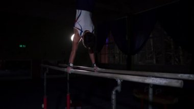 Erkek jimnastikçi acrobat paralel bar yavaş bir takla paylaşımı ve yere iniş karanlık bir odada amut gerçekleştirir. Olimpiyat Oyunları nda önce eğitim