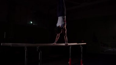 Spor giyim, karanlık bir odada profesyonel jimnastikçi kerevit paralel bar üzerinde duruyor ve flips ağır çekimde gerçekleştirir. Olimpiyat Oyunları için hazırlık zor eğitim