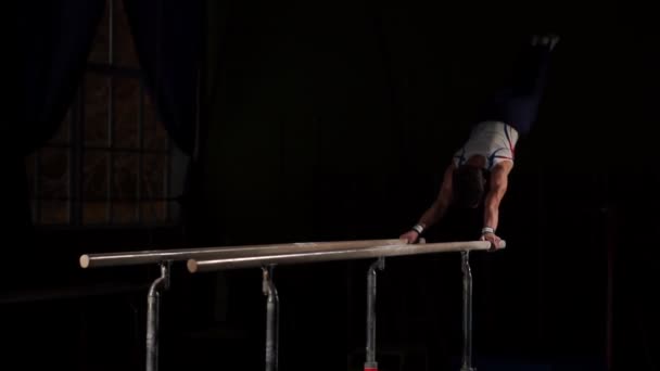 Manliga gymnast acrobat utför handstående på barr i ett mörkt rum i slow motion — Stockvideo