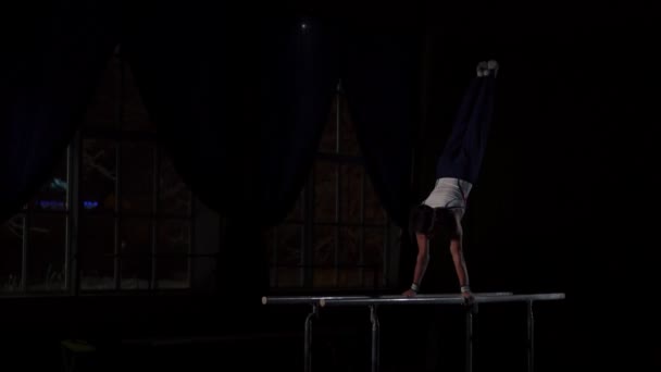 Mannelijke Turner acrobat voert handstand op parallelle staven in een donkere kamer in slowmotion delen flips en de landing op de verdieping — Stockvideo