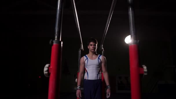 Spor giyim, karanlık bir odada profesyonel jimnastikçi kerevit paralel bar üzerinde duruyor ve flips ağır çekimde gerçekleştirir — Stok video
