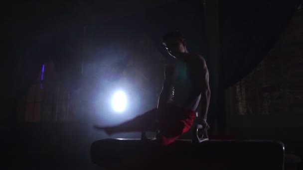 Erkek jimnastikçi kulplu beygir spin performans üzerinde Olimpiyat programdan egzersizleri yapar ve yavaş eğitim zor duman etrafında karanlık odada Olimpiyatları için hazırlık alır ve — Stok video