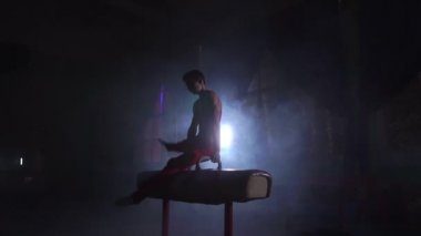Karanlık bir odada duman yavaş çekimde kulplu beygir egzersiz erkek jimnastikçi gerçekleştirir. Spor Sağlık ve başarı için