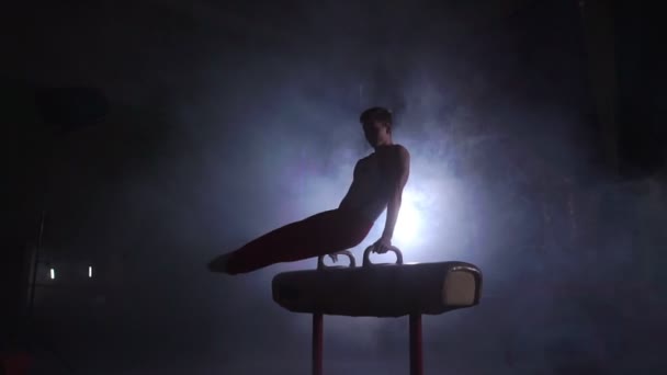 Gimnasta masculino realiza ejercicio de caballo Pommel en una habitación oscura en el humo en cámara lenta. Deportes para la salud y el logro — Vídeo de stock