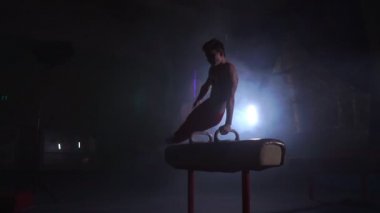 erkek jimnastikçi atlet amut ve spin kulplu beygir koyu arka planı ve duman yavaş hareket üzerinde gerçekleştirir. Olimpiyat programı. Egzersiz için hazırlık