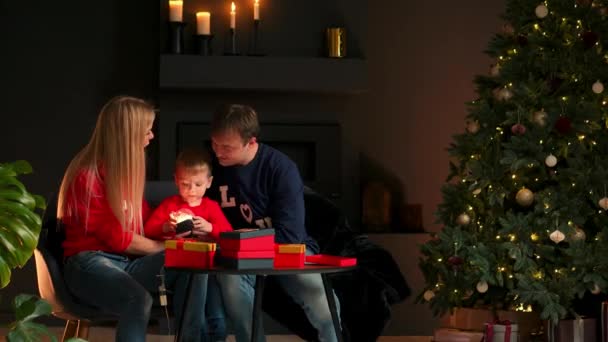 Portret szczęśliwy rodziny otwierając prezent na Boże Narodzenie obecny opakowania w godzinach wieczornych. Koncepcją z niespodzianka, szczęśliwa Rodzina, święta, e-commerce, zakupy online. — Wideo stockowe