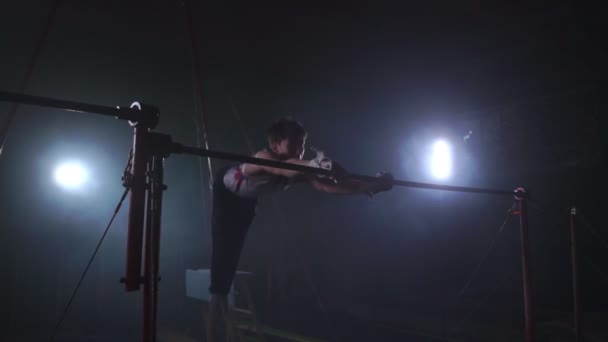 Turner auf dunklem Untergrund an der Querstange dreht sich und springt in Zeitlupe und um den Rauch herum über sich selbst — Stockvideo