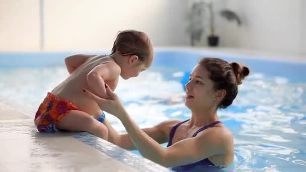 Mãe ajuda o bebê a ficar do lado da piscina durante o treinamento de natação para bebês — Vídeo de Stock