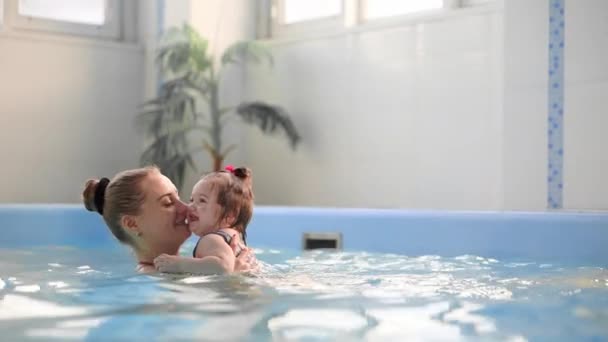 Schöne Mutter bringt süße Baby-Mädchen bei, wie man in einem Schwimmbad schwimmt. Kind vergnügt sich mit Mama im Wasser. — Stockvideo