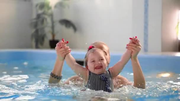 Carino bambino biondo in occhiali protettivi si sta tuffando sott'acqua insieme a sua madre in piscina cercando di tirare fuori il suo giocattolo. Sua madre gli sta insegnando a nuotare. Un colpo subacqueo — Video Stock