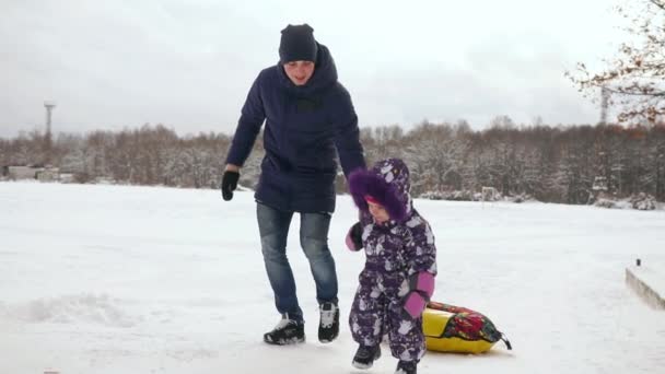 Папа толкает её дочь на резиновую надувную снежную трубку в замедленной съемке. — стоковое видео