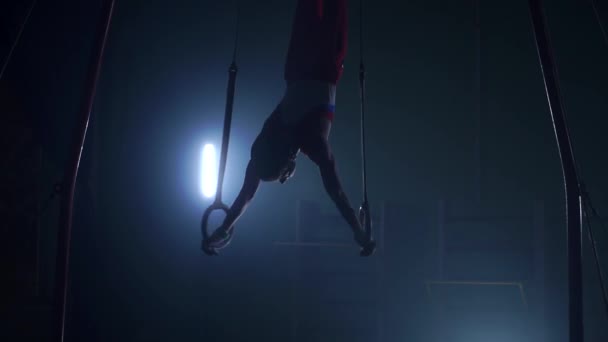 Gymnast on a dark background stands on his hands using rings in the air. Performs rotation in the Olympic program — Stock Video