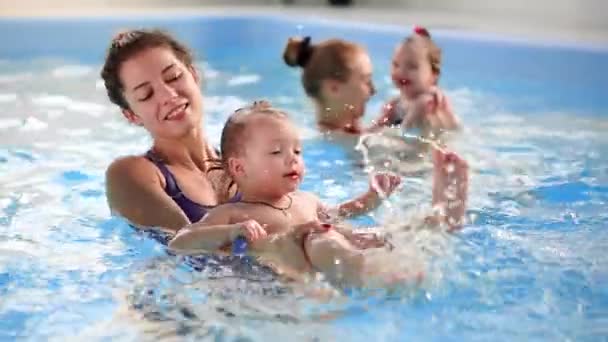 Happy middle-aged mother swimming with cute adorable baby in swimming pool. Smiling mom and little child, newborn girl having fun together. Active family spending leisure and time in spa hotel. — Stock Video