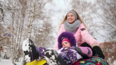 Mutlu anne ve kızı kışın karda kızakla ve kartopu oynarken. Anne ve çocuk gülmek ve şişirilebilir tüp glide sevinirler. Park Noel tatili sırasında oynamaya aile. Ağır çekim.