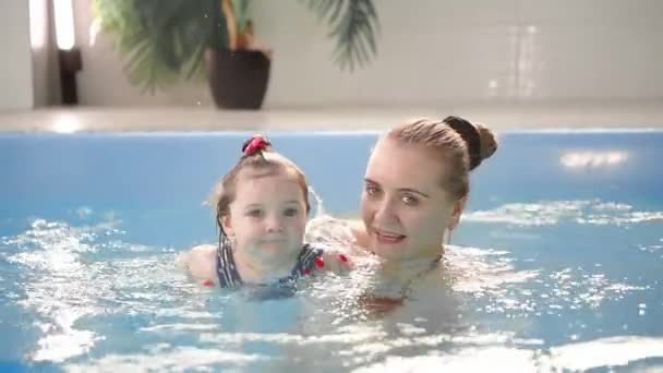 Hermosa madre enseñando linda niña cómo nadar en una piscina. Niño divirtiéndose en el agua con mamá . — Vídeos de Stock