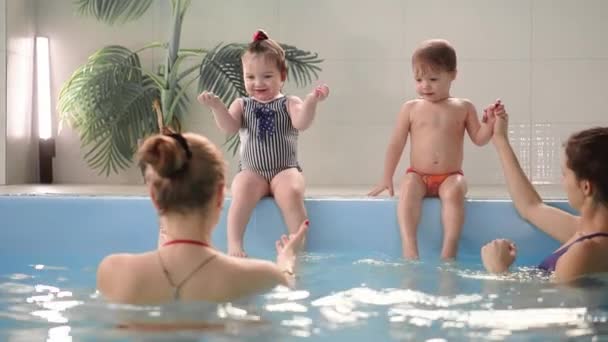 Двоє дітей сміються в басейні і стрибають у воду, плескаючи руками — стокове відео