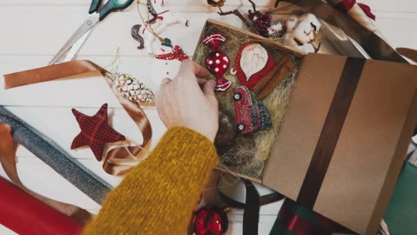 Aerial footage of woman tying red ribbon on gift. Lockdown shot of female packing present at wooden table. Overhead flat lay of art and craft equipment surrounding ladys hands. — Stock Video