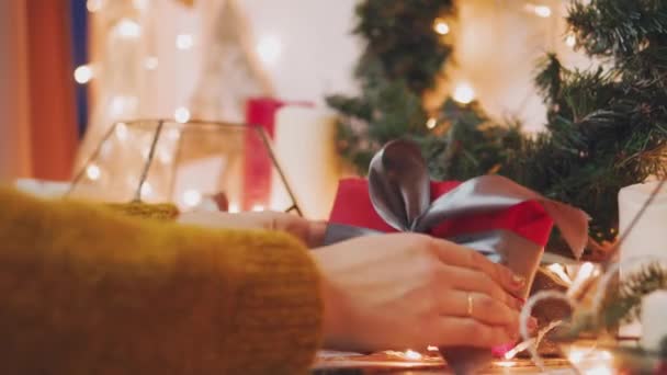 Un hobby creativo. Confezione regalo. Confezione regalo natalizio moderno scatole in elegante carta grigia con nastro rosso satinato. Vista dall'alto delle mani su tavolo in legno bianco con rami di abete, decorazione — Video Stock