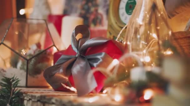 Beautiful gift in the hands of men. New Years gift with a red ribbon, fir on the table. The man made it himself and is going to give for the holiday. Beautiful background with fireplace. — Stock Video