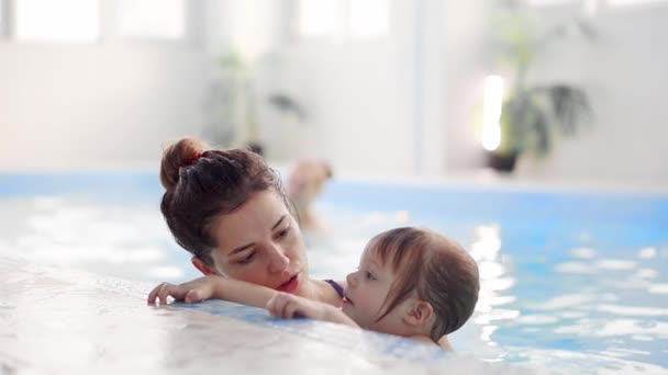 Ребенок в бассейне прыгает со стороны в воду и плавает к своей матери в замедленной съемке — стоковое видео