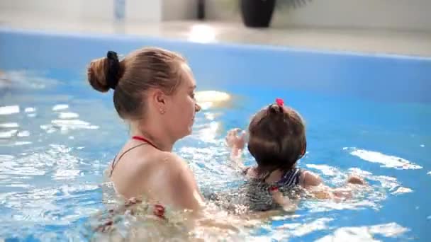 Jovem mãe na piscina brincando com sua filha bebê em câmera lenta. Família de esportes envolvidos em um estilo de vida ativo — Vídeo de Stock