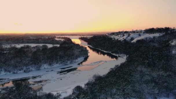 Ηλιοβασίλεμα πάνω από παγωμένος ποταμός και καταπράσινα δάση. Χώρα εθνική οδό περνώντας κατά μήκος του νερού στο χειμώνα. — Αρχείο Βίντεο