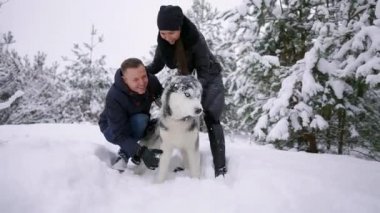 Aile portre sevimli mutlu çiftin yalama alaskan malamute köpekleri ile sarılma yüz mans. Komik köpek yavrusu Santa giyen Noel geyik boynuzları ve öpüşme kadın. Özgürlük yaşam tarzı evde beslenen hayvan aşık.