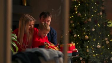 Aile Anne baba ve oğul evde açık hediyeler Noel, Noel iç kanepede oturuyor. Sıcak ve rahat ev atmosfer