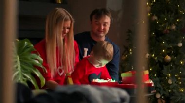 Neşeli Noel ve mutlu tatil neşeli sevimli çocuklara ve ailelerine hediye açılış. Eğleniyor tree yakınındaki sabah pijama giymiş çocuk. Sevgi dolu aile ile odada sunar.