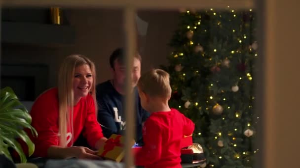 Mamma papà e figlio a Natale aprono i regali a casa seduti sul divano all'interno di Natale. Atmosfera calda e accogliente — Video Stock