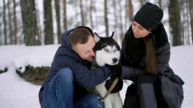 Bir adam ve bir kadın bir köpek kış orman gülümseyen içinde Siberian dış yapraklar sarılma ve birbirimize ve kamera bakarak oturuyordu. Ağır çekim