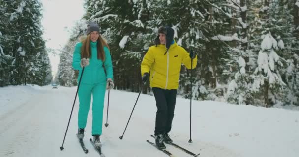 Улыбающийся мужчина в зимней куртке катается на лыжах в лесу в замедленной съемке со своей любящей женой. Здоровый образ жизни. Молодая пара — стоковое видео