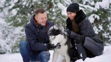 Aile portre sevimli mutlu çiftin yalama alaskan malamute köpekleri ile sarılma yüz mans. Komik köpek yavrusu Santa giyen Noel geyik boynuzları ve öpüşme kadın. Özgürlük yaşam tarzı evde beslenen hayvan aşık.
