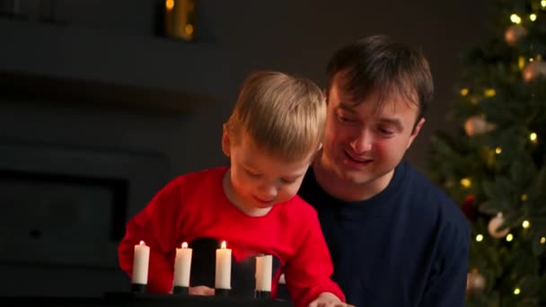 Famille à Noël assis sous le sapin en regardant l'enfant souffle les bougies et rit. Maman et papa rient et sourient — Video