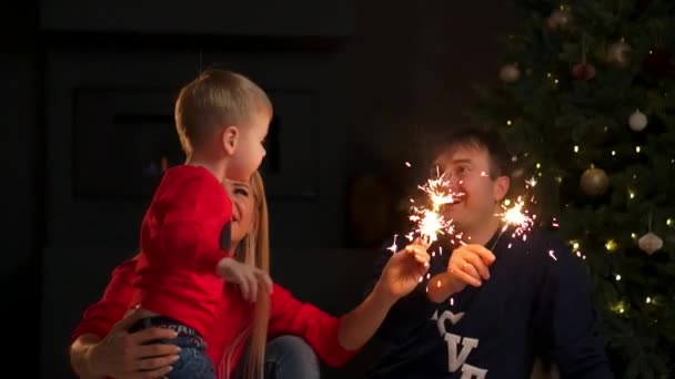 Familia feliz y fuego de Bengala por la noche. Madre sosteniendo chispa, entonces ella y el padre besar al niño mientras que él mirando la luz que sale al final — Vídeo de stock