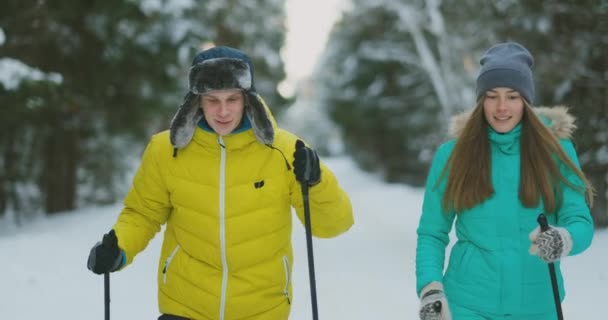 Smiling girl in blue jacket skiing rides in the woods with her boyfriend in winter on the eve of Valentines day. slow motion. — Stock Video