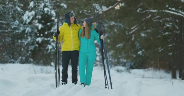 Retrato completo de un joven cariñoso ayudando a su novia lesionada durante el paseo de esquí en el bosque de invierno — Vídeos de Stock