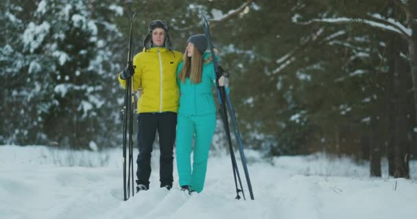 Visão lateral retrato de jovem casal ativo carregando esquis conversando no caminho de volta na bela floresta de inverno, espaço de cópia — Vídeo de Stock