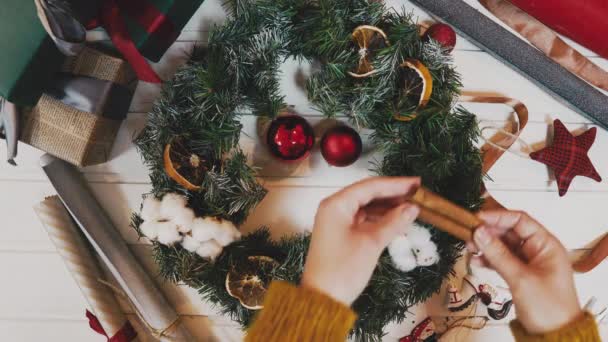 Vista superior de las manos femeninas que sostienen la corona de Navidad con ramas de abeto y bayas decorativas, con la palabra Navidad en la mesa de madera — Vídeo de stock