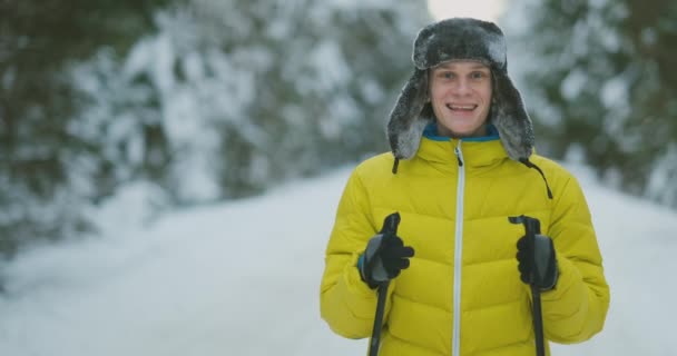 Homem sorridente com esquis e sua esposa olhando para algo curioso durante a viagem na floresta de inverno — Vídeo de Stock
